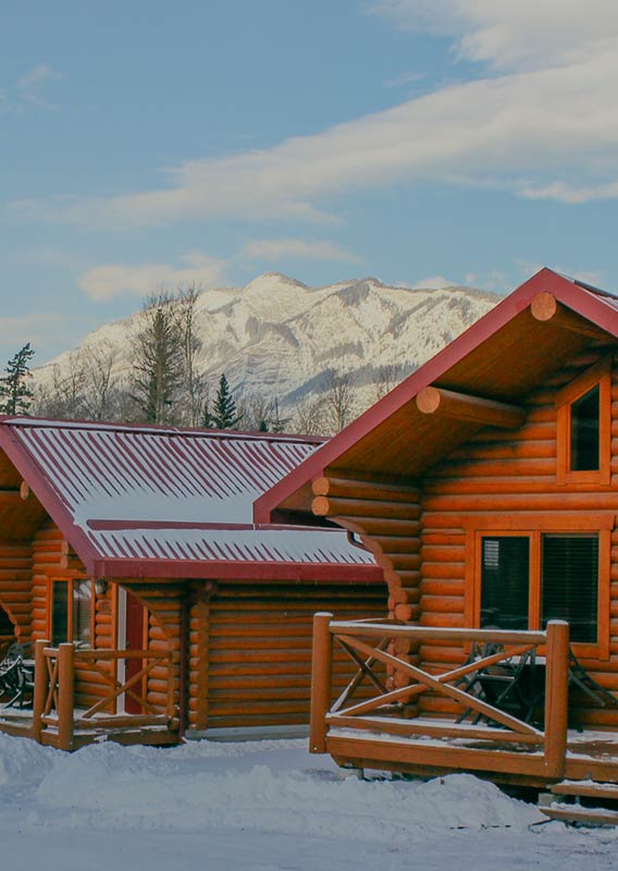 A row of cabins in the winter with mountains in the background.