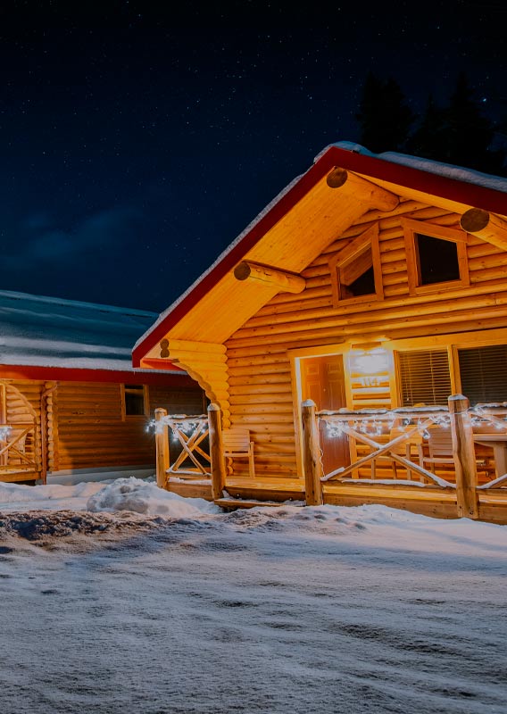 Wooden cabins with red roofs covered in snow, lit up in the night.