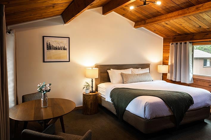 A bed in a hotel room with a wide window and small table