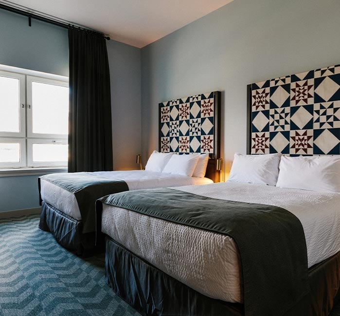 Two hotel beds in a room with a large sunny window.