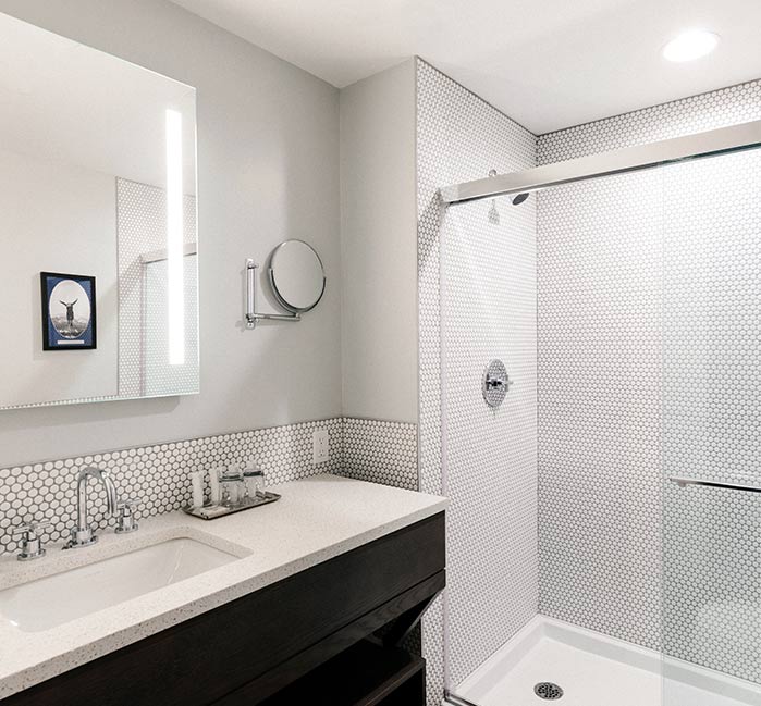 A hotel bathroom with a long sink counter and glass shower.