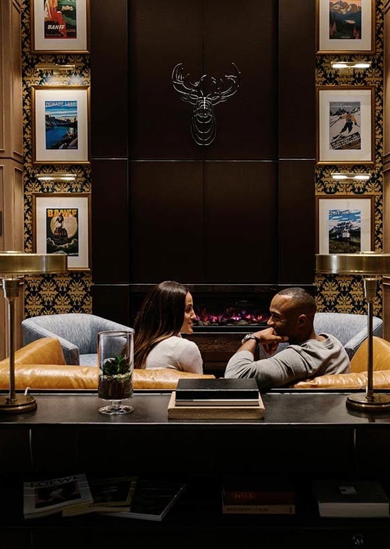 People sit on a couch in front of the large fireplace in the Mount Royal Hotel lobby