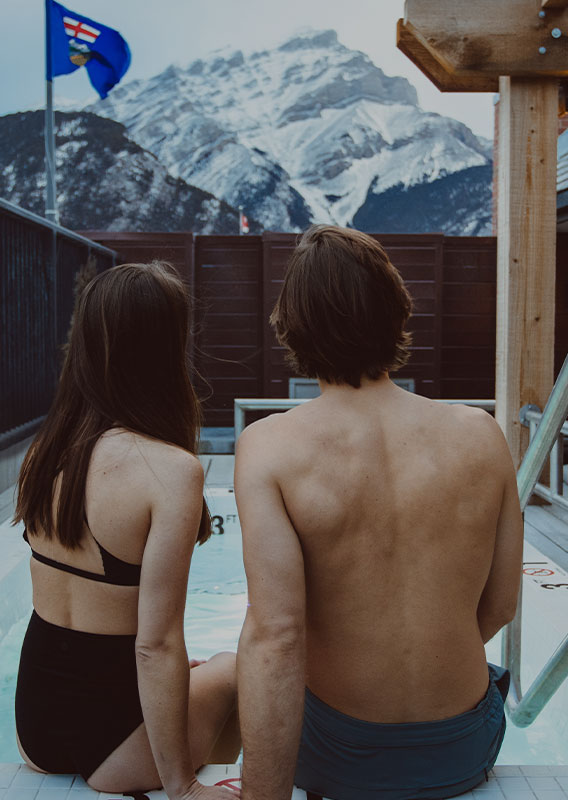 People enjoy the rooftop hot tubs at the Mount Royal Hotel with Cascade Mountain behind them