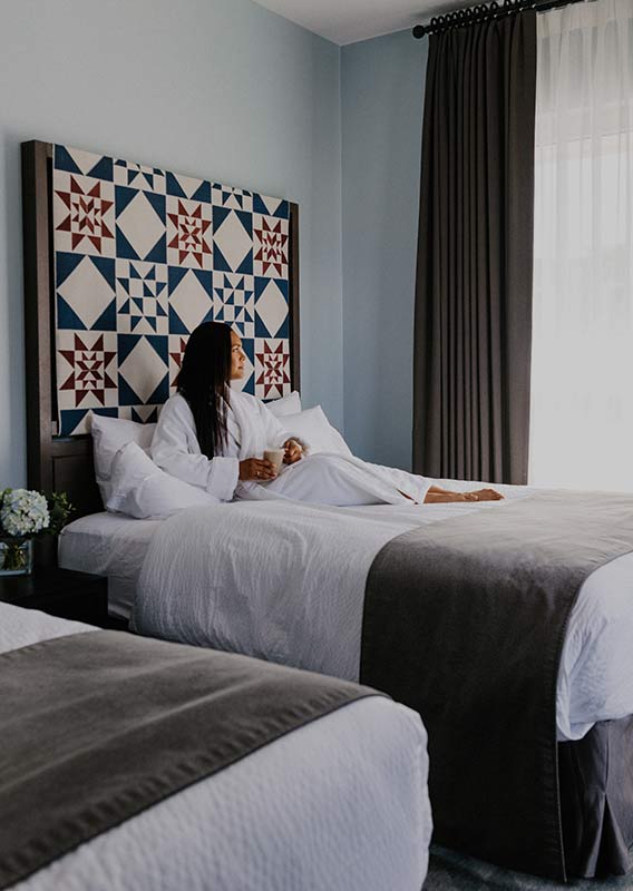 Woman lounges in robe drinking a latte on bed looking out large window