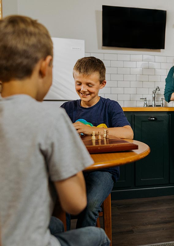 A family relaxes in a cabin kitchen. Children play chess.