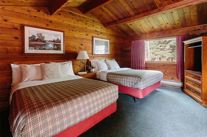 Two beds in a hotel room with a wide window with a view to a forest