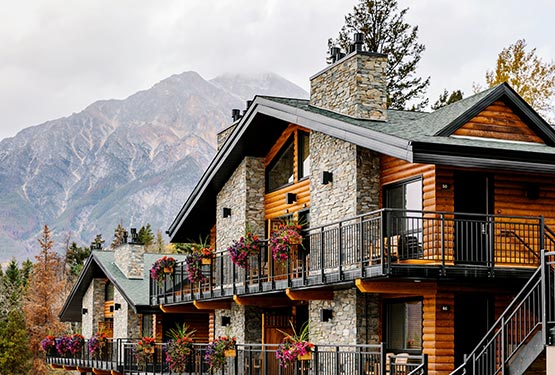 A wooden and stone lodge below tall mountains.