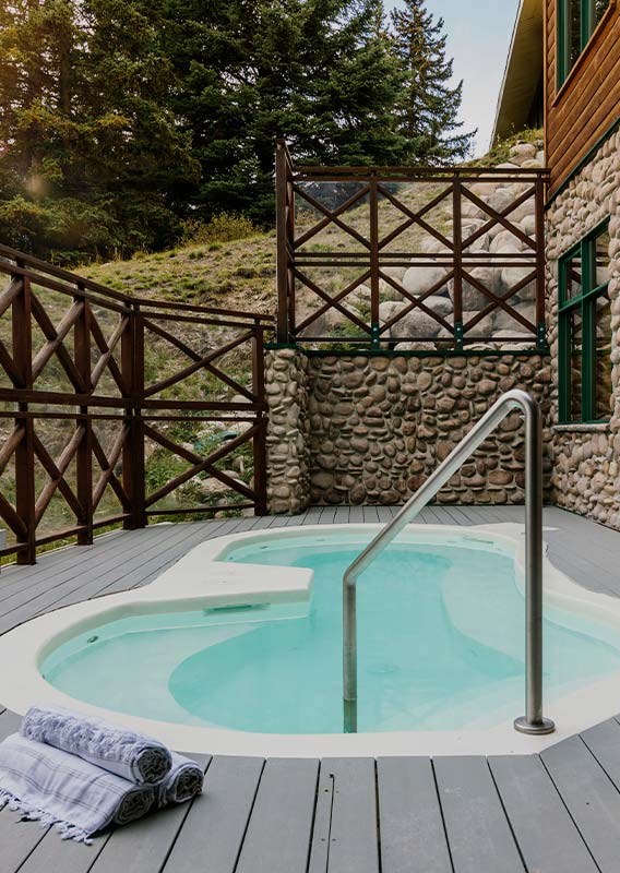 A hot tub on a wooden deck with stone and wooden fencing around.