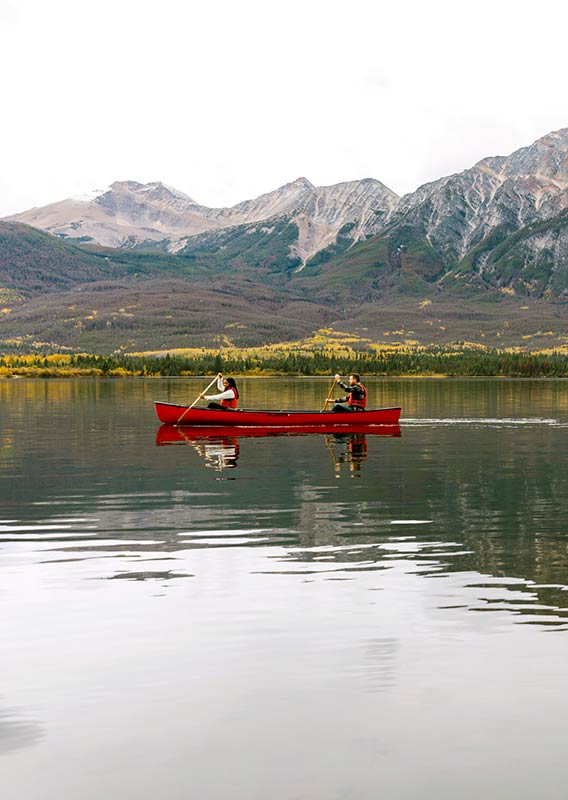 Two people padding in a red canoe over a still lake with a mountain range in the background.