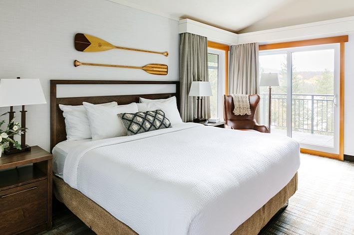 A bed in a hotel room with wide doors leading to a balcony