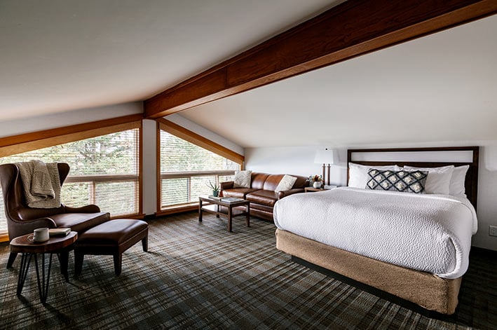 A king bed in a loft room with couch and lounge chair by the wide window