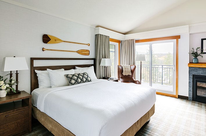 A bed in a hotel room with a forest view from the balcony