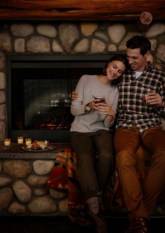 Two people relax by a fireplace.