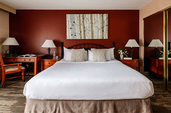 A bed in a hotel room with red accent wall