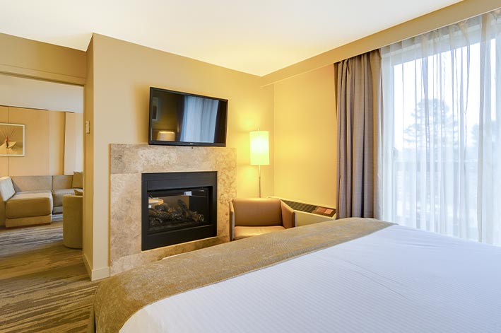 A hotel room bed facing a fireplace and television