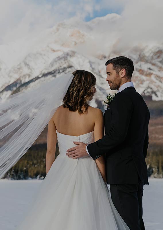 A bride and groom stand outside in the snow