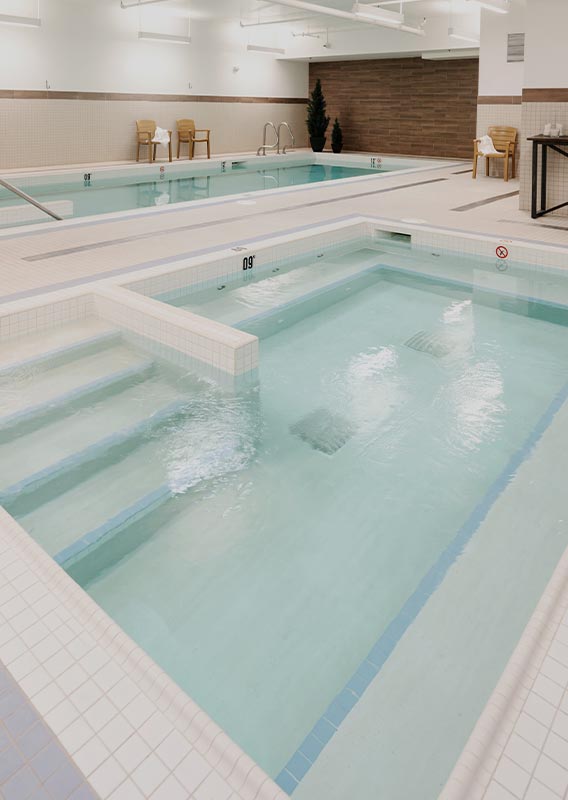 A pool and hot tub in a tiled room.
