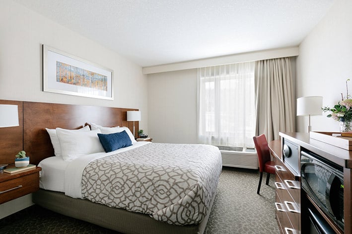 A queen bed in a hotel room with colourful art above the headboard.