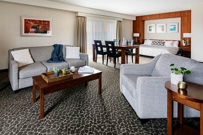 A living area in a hotel suite with couch, tables and a bed in the back.