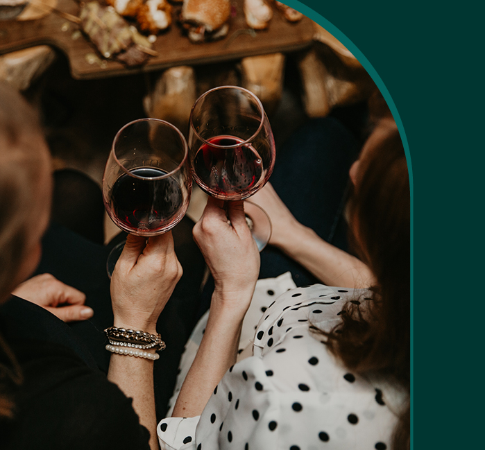 A view from above of two women cheering glasses of red wine, with a text graphic overlaid that says "Cheer"