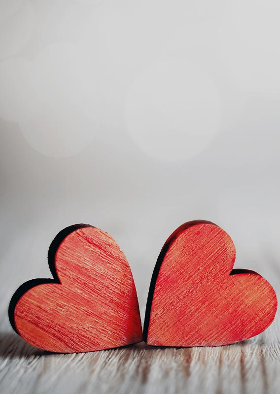 Two red wooden hearts arranged on a beige backdrop.