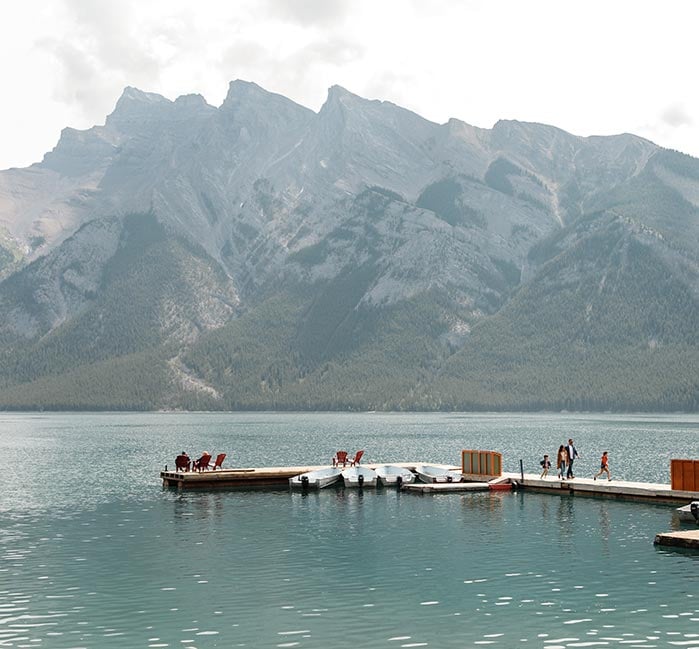 A dock out on a blue lake below mountains.