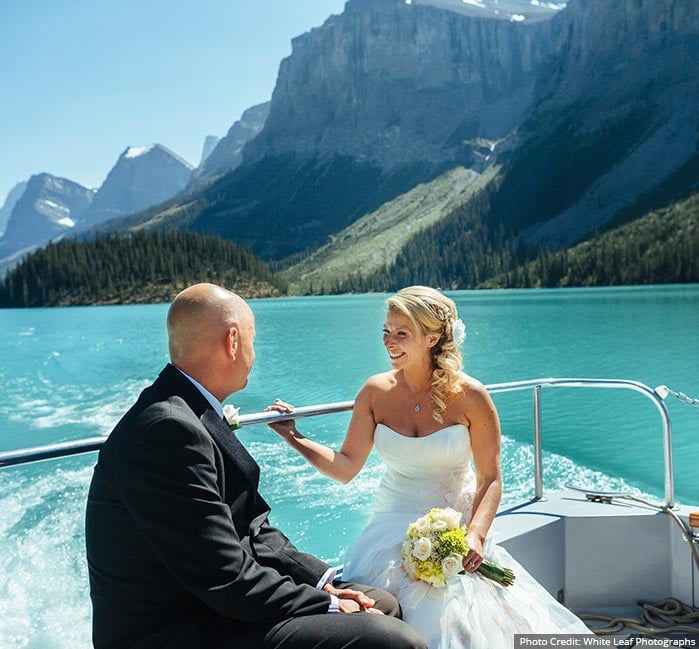 A couple look at each other while seated at the back of a boat on Maligne Lake.