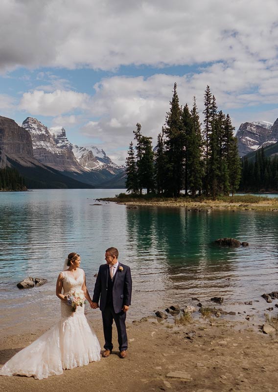 A bride and groom pose on a frozen Pyramid Lake at the base of a snowy mountain