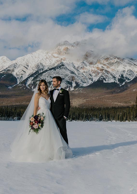 A newly wed couple stands on a snowy frozen lake.