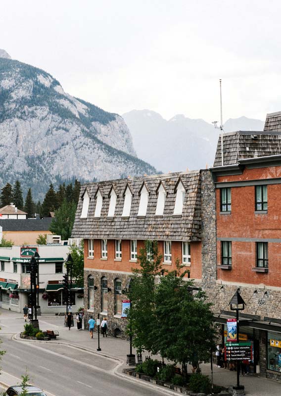 The outside of the Mount Royal Hotel, a red brick and stone building, with mountains behind it.