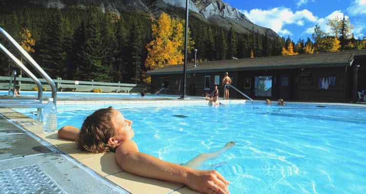 A woman relaxes in a hot springs pool below mountains