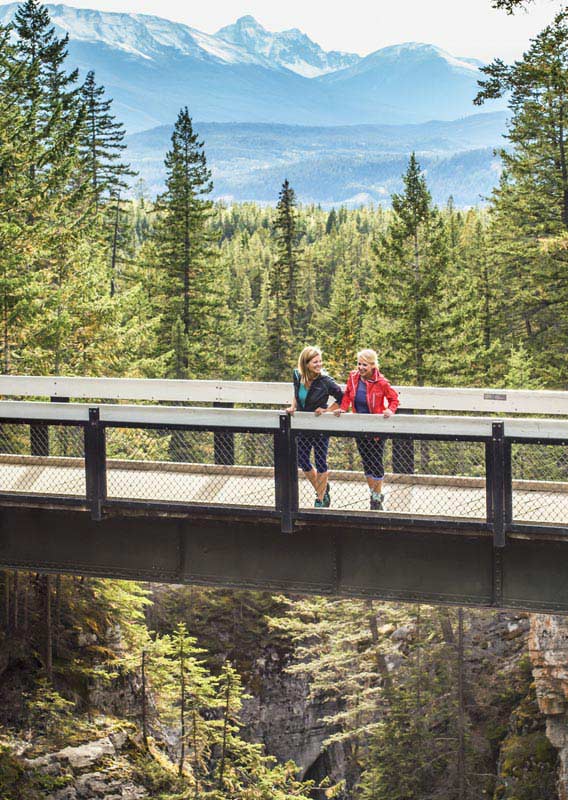 Two women stand on a bridge overlooking a rocky canyon