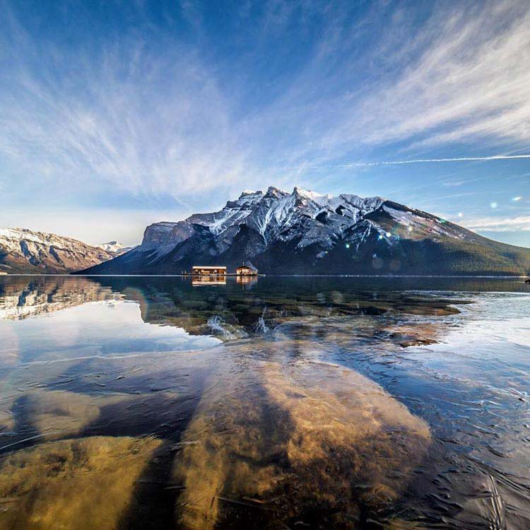 A view of Lake Minnewanka, looking towards snow-covered mountains and wispy clouds.