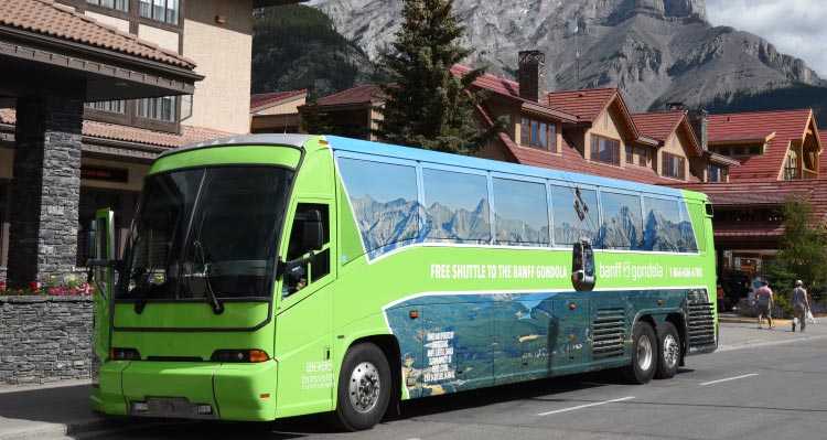 A green bus is parked on a street with mountains rising behind the streetscape.