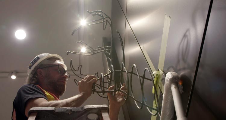 Jame Greisinger hangs his artwork, a steel-rod deer trophy on a wall.