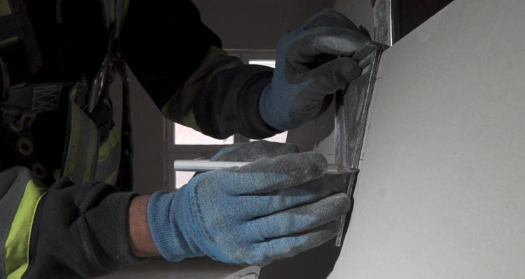 A worker wearing blue gloves cuts drywall