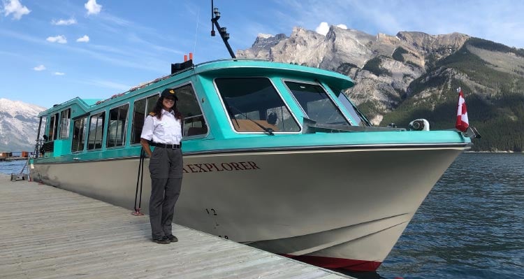 A boat captain stands on a dock next to a blue and white boat.