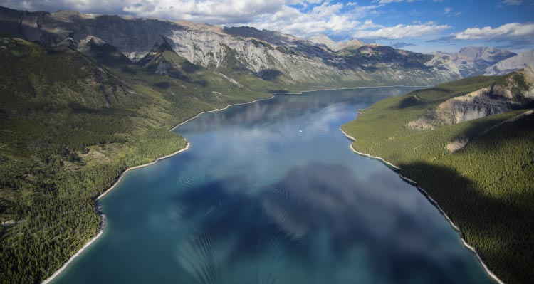 An aerial view of a large blue lake between tree-covered mountains.