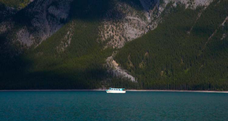 A boat cruises on a blue lake with a green mountainside behind it.