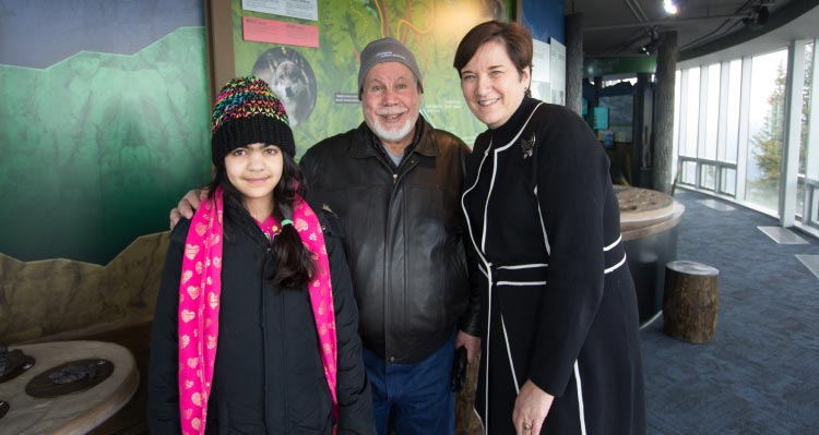 Three people smile and pose for a photo next to an interpretive display.