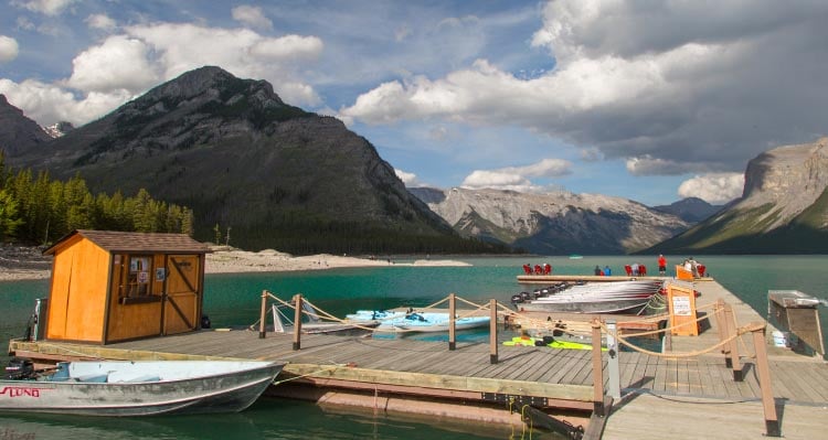 Boats are docked on a large blue lake, below tree-covered mountainsides.