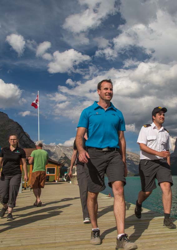 A group of Lake Minnewanka Cruise crew members walk down a wooden dock.