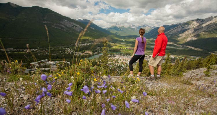 Two people overlook a town in a wide green valley.