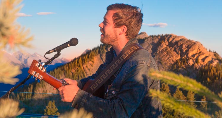 A musician sings and plays guitar atop a mountaintop.