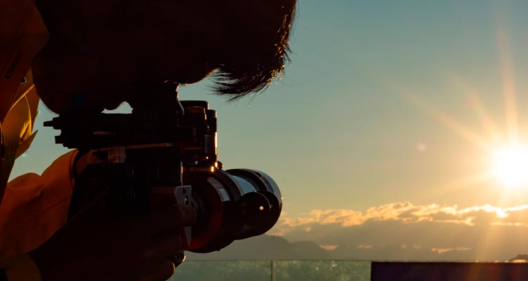 A person looks through a solar telescope pointed towards the setting sun.
