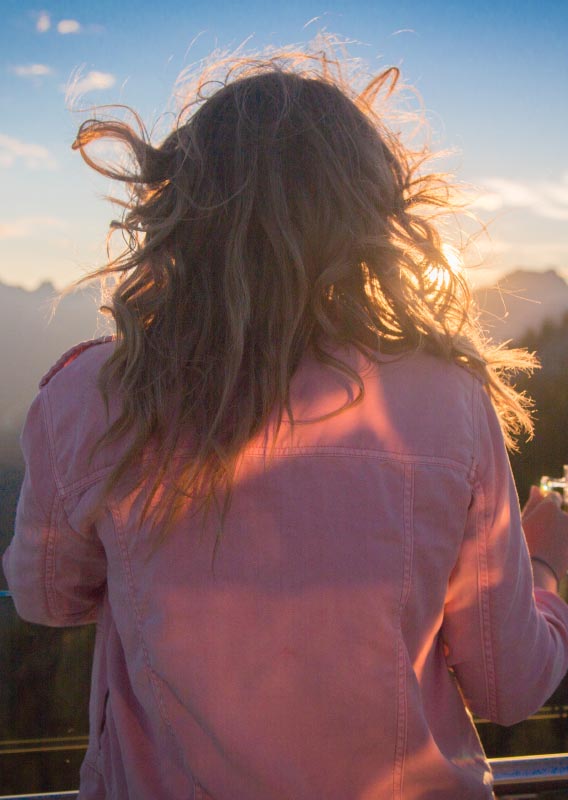 The sunset glows behind a person looking out over a mountain range.