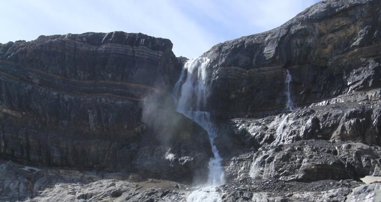 A waterfall descends along a striped rockface