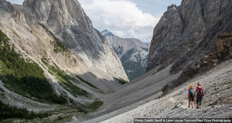 Hikers walk into a narrow valley  between steep mountainsides.