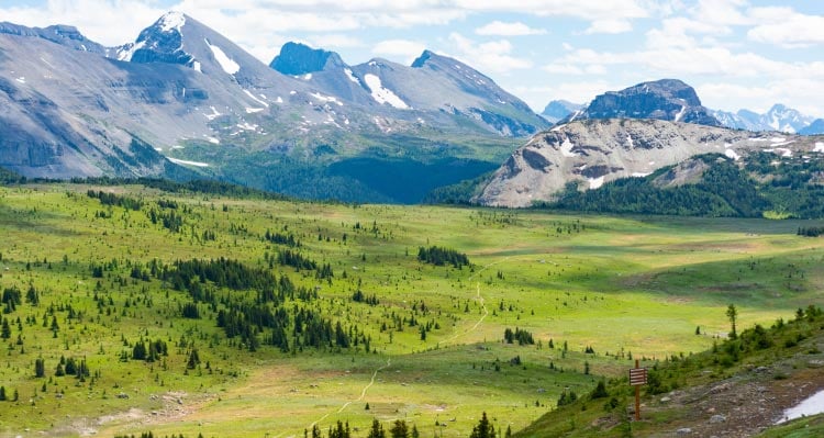 A wide green alpine meadow stretches between high rocky mountains.