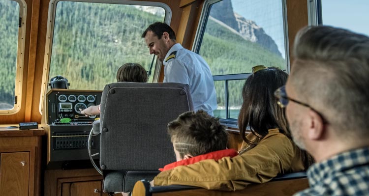 A child sits in the captain's chair of a boat with the boat captain.